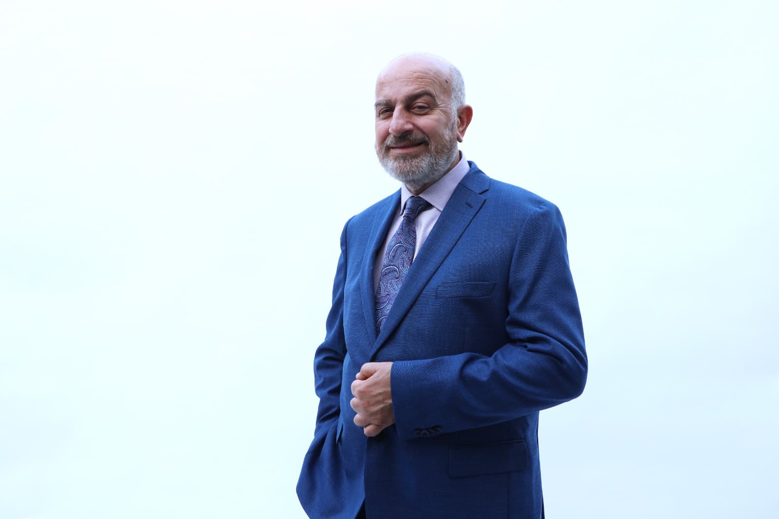 Serge Khatchadourian smiling in a blue suit with his hands clasped