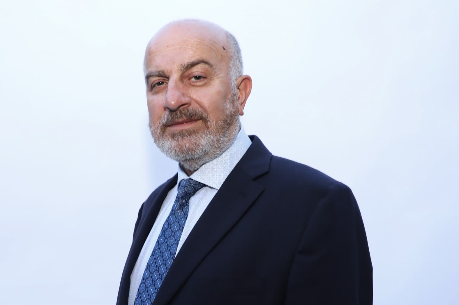 Close portrait of Serge Khatchadourian in a dark navy suit and blue patterned tie
