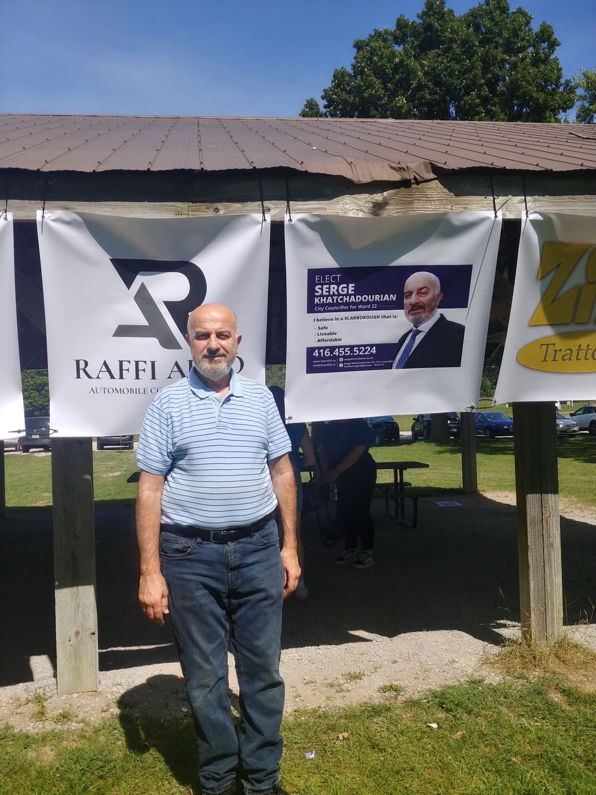 Serge Khatchadourian at an outdoor community picnic beside his campaign banner