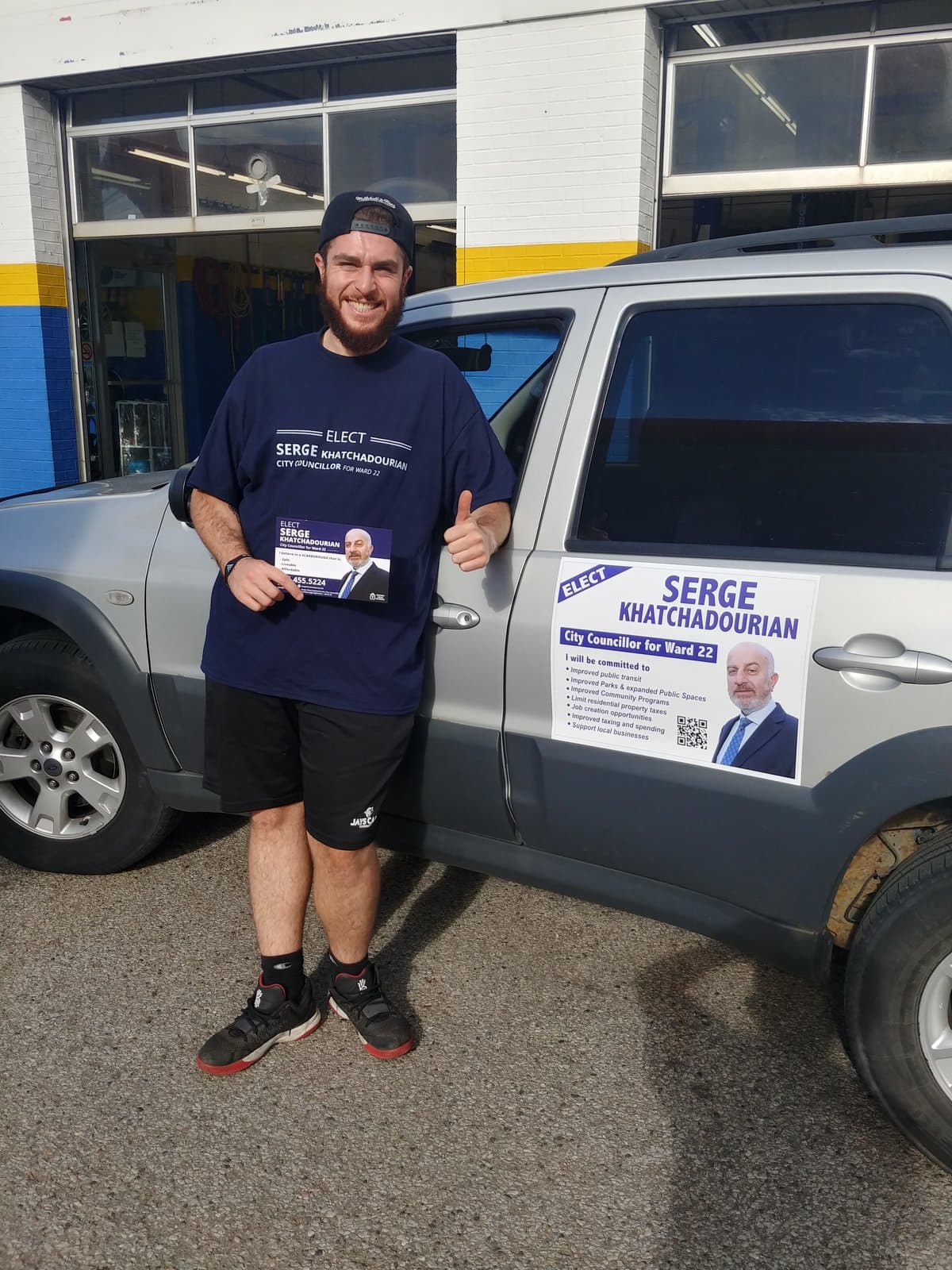 A campaign volunteer beside a vehicle carrying a Serge Khatchadourian campaign sign